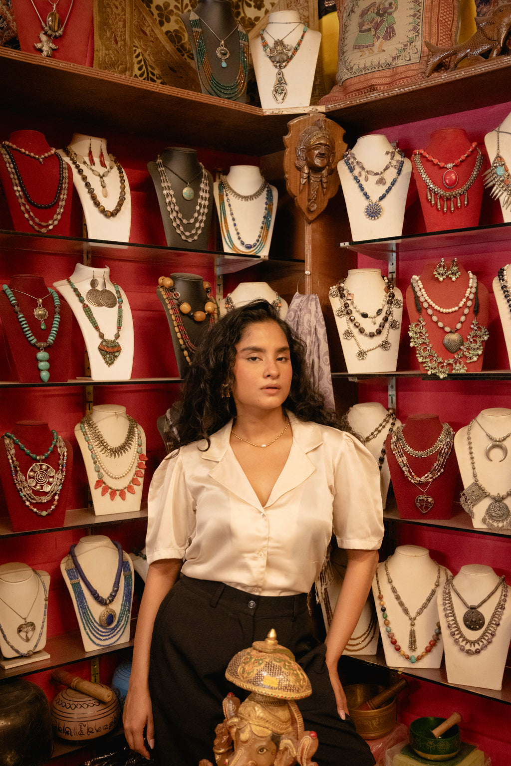 Woman standing in front of a jewelry display with various necklaces on mannequins.
