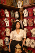 Woman standing in front of a jewelry display with various necklaces on mannequins.