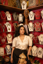 Woman standing in front of a jewelry display with various necklaces on mannequins.