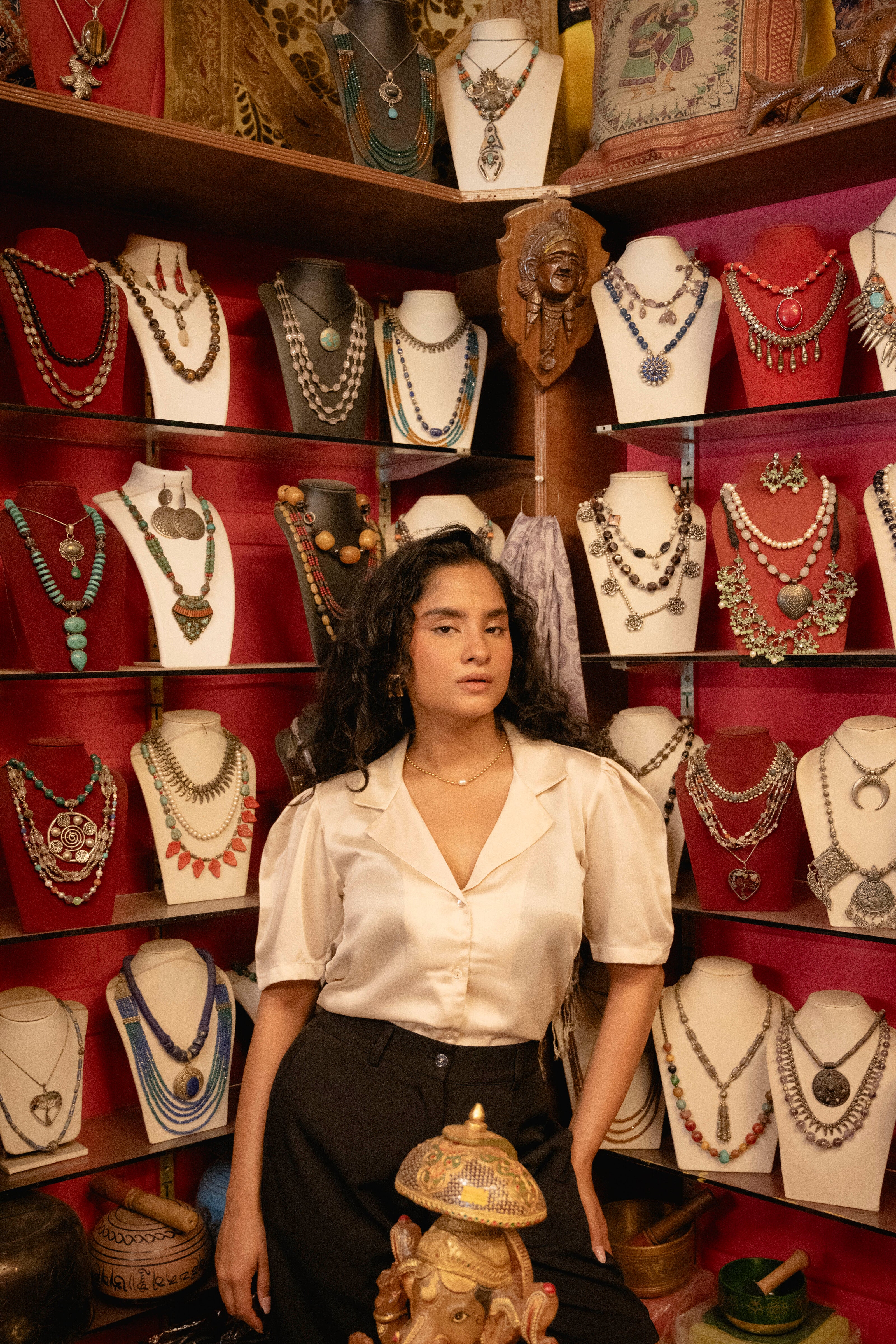 Woman standing in front of a jewelry display with various necklaces on mannequins.